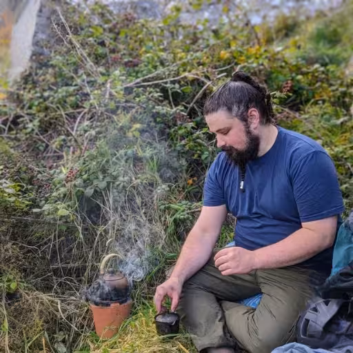 Duncan Davis of INFUSE Bodyworks, sitting outdoors brewing tea on a small stove